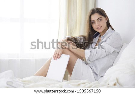 Portrait of woman using tablet and drinking coffee while sitting on the bed in the morning