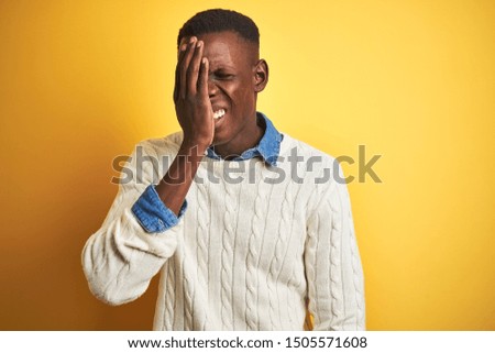 African american man wearing denim shirt and white sweater over isolated yellow background Yawning tired covering half face, eye and mouth with hand. Face hurts in pain.