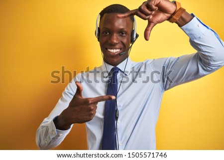 African american operator man working using headset over isolated yellow background smiling making frame with hands and fingers with happy face. Creativity and photography concept.