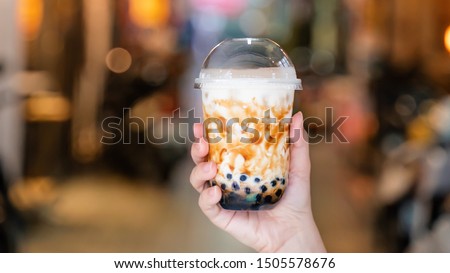 Young girl is holding and showing a cup of brown sugar flavored tapioca pearl bubble milk tea in night market of Taiwan background, close up, bokeh Royalty-Free Stock Photo #1505578676