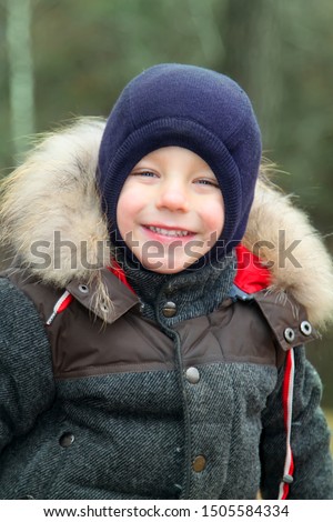 happy smiling boy in warm clothes and hat covering his neck from cold wind llooking at camera in autumn outdoor