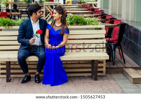 long haired brunette indian woman in blue dress with her handsome boyfriend having dating .man giving rose to his girlfriend in summer downtown street.