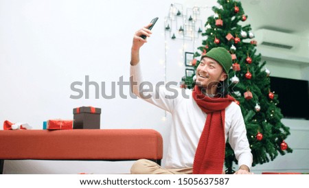 Young asian man take selfie, video call by smart phone while sitting in Christmas celebration party at home with happiness