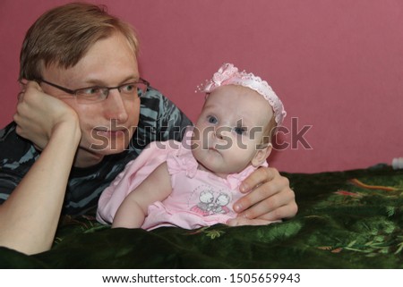 Dad plays and holds a little daughter in his arms. Baby and father. Family in the room on a pink background.
