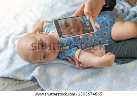 Mother is taking a picture of her baby by a smart phone closeup. Detail of her son's face is on smart phone screen. All potential trademarks are removed. 