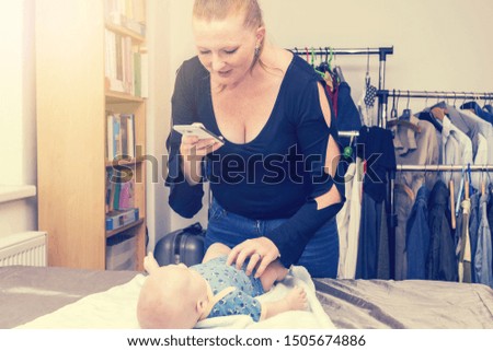 Mother taking a picture of her baby by a smart phone. Mother is holding son's body and smiling. Concept photo of parenthood and motherhood