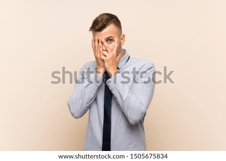 Young blonde businessman over isolated background covering eyes and looking through fingers