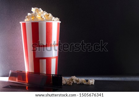Bucket of salty popcorn and film stock against dark background.Darkness at the cinema