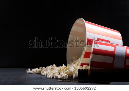 Scattered popcorn, big buckets and film stocks on th grey surface against black background