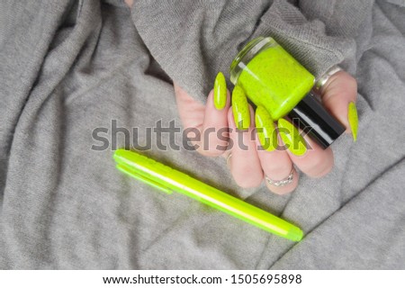 Female hand with long nails and a bottle of neon emerald green nail polish