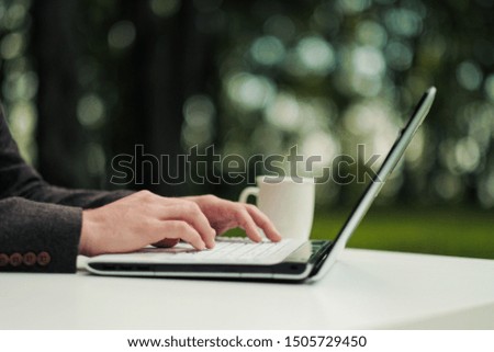 Close-up of male hands on a laptop keyboard. Outdoor business and work concept. Copy space on a green blurred background.