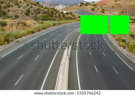 Tight frame overview of an empty, two way six lanes, curved highway in a countryside hill surrounding with two green screen direction signs for copy space.