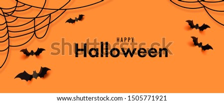 Creative scary composition of black paper bat with spider web on orange background. Autumn holiday composition.