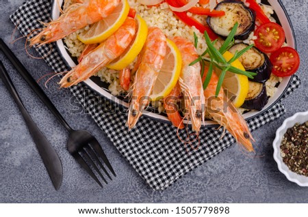 Unpeeled boiled shrimp with bulgur and vegetables in a dish on a slate background. Selective focus.