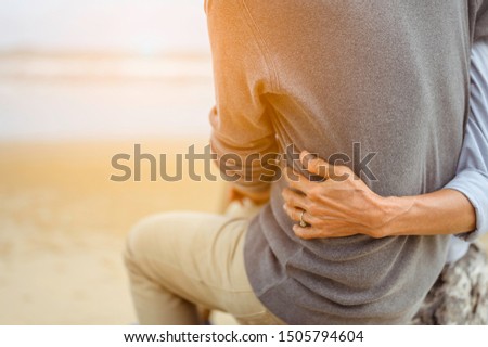 Retirement couple  on a summer evening watch sea, Woman hugging her husband at the beach at sunset.