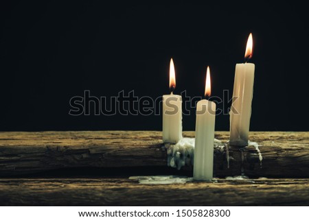 Beautiful three white burned candles on a old oak wooden table and black background. 