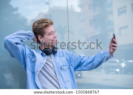 A smiling man with glasses and headphones taking a picture of himself with his smartphone. Concept of technological youth. Portrait