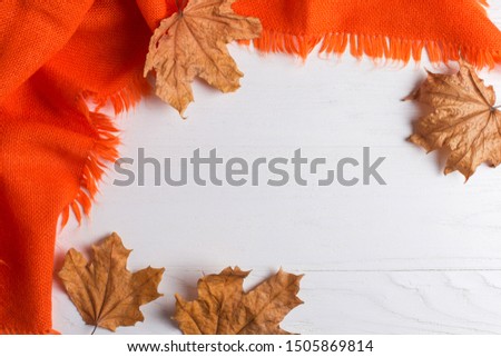 Bright orange warm shawl, pumpkins and dry yellow leaves on a white background, autumn mood, copy space.