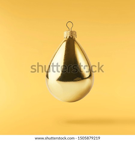 Christmas card conception. Christmas gold bauble falling in the air on yellow background. Levitation concept. High resolution image