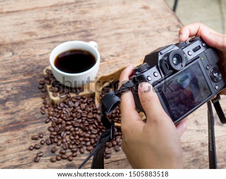 The photographer is intending to use digital camera take pictures a cup of blak coffee and coffee beans.