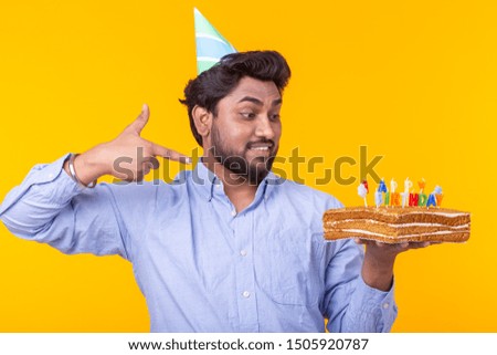 Positive young man holding a happy birthday cake posing on a yellow background.
