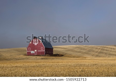 A red barn stands in a harvested field with the lifting fog in eastern Washington.