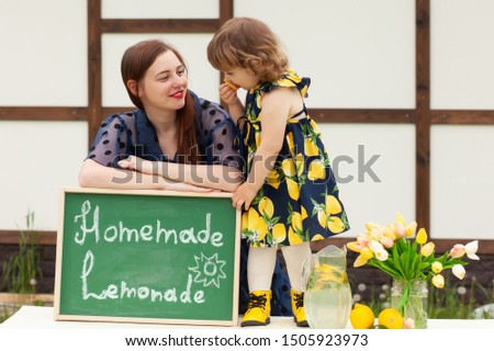 Happy family of mother and daughter having fun selling lemonade outdoors, sunny summer day