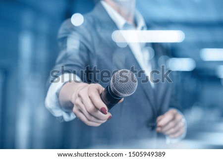 The speaker holds a microphone on a blurred background.