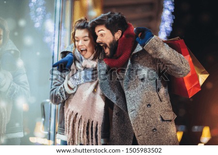 Couple with gift bag on Christmas lights background during walking in the city at evening. Selective focus.