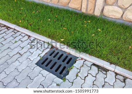 Plastic drain gutter, green grass lawn and stone pavement sidewalk.