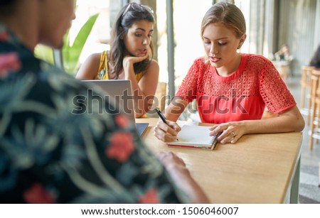 Candid lifestyle shot of group of diverse millennial employees brainstorming together on laptop computer in bright modern restaurant