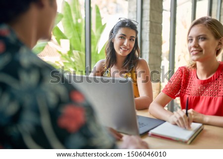 Candid lifestyle shot of three multi-ethnic millennial colleagues collaborating together on laptop computer in bright modern cafe