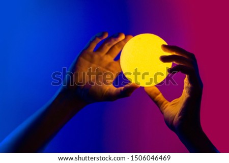 Man holding yellow moon shape illuminated sphere. Surrealistic photo style, contemporary art element for design, posters and banners. Neon blue and purple light.
