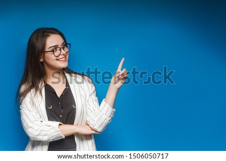 Pretty girl, teacher in eyeglasses show something isolated on blue background. Copy space. Place for text.