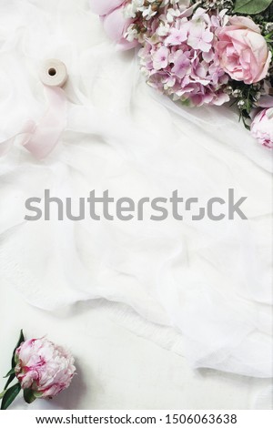 Feminine floral frame composition. Beautiful pink peonies, hydrangea and roses flowers on white muslin table runner background. Empty space. Wedding styled stock photo. Vertical flat lay, top view.