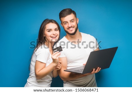 Portrait of a two happy young men and woman  holding laptop computer while standing with credit card and celebrating isolated over blue background. Online shopping.