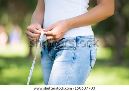 Healthy unrecognizable woman with measure tape on nature background measuring waist