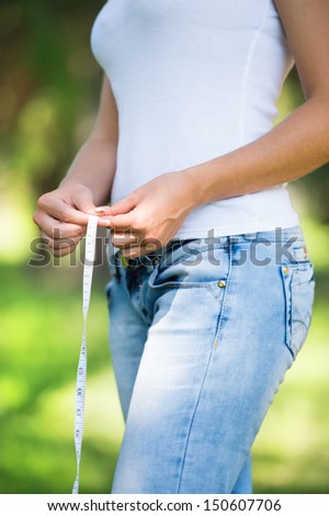 Healthy unrecognizable woman with measure tape on nature background measuring waist