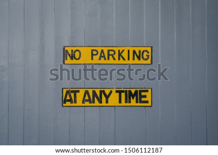 No parking at any time yellow sign on a grey wooden garage door. 