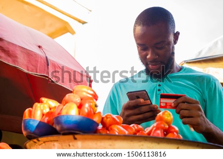 young black man making some payments with his card on his phone in the market