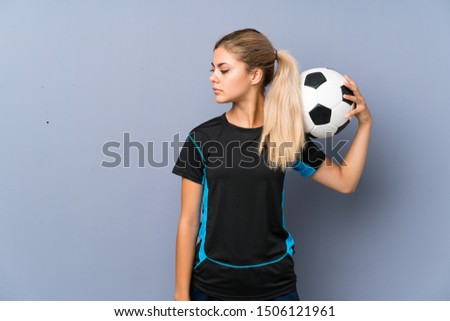 Blonde football player teenager girl over grey wall