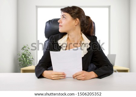 Young female business employee newly hired or a student doing writer internship.  She is in a workstation in a corporate office holding paper documents.