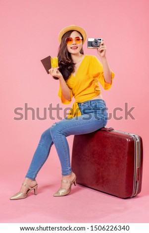 Smiling woman traveler sitting on luggage holding camera passport credit card in holiday on pink backgrounds, relaxation concept, travel concept
