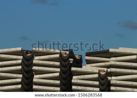 Pre cast concrete curved road tunnel segments stacked in a pile at a warehouse site. Precast plant. A blue sky background