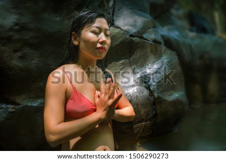 young beautiful and happy Asian Chinese woman enjoying unique Summer holidays at tropical forest meditating doing yoga pose relaxed in natural pool delighted by magical feeling at jungle lake