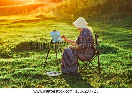 an elderly woman paints a picture in nature