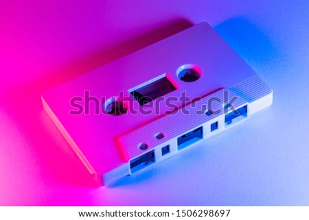White audio cassette tape lit by pink and blue lamps on a white background. 