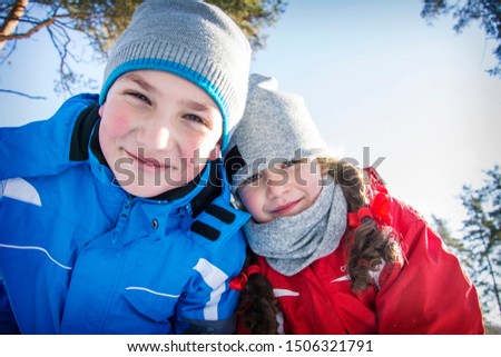 In winter, in the forest on a bright sunny day, happy brother and sister are standing in an embrace. Close-up.