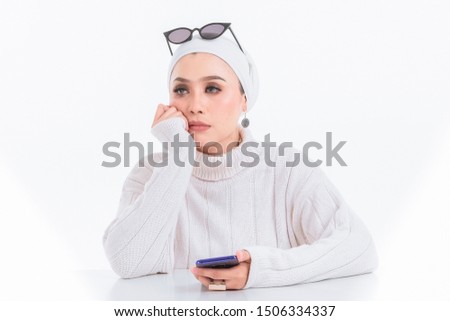 A beautiful muslim girl wearing white hijab and white shirt with sunglasess while using phone. isolated white, studio background.