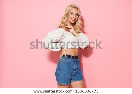 Image of caucasian blonde woman with long curly hair wearing trendy clothes smiling and looking at camera isolated over pink background